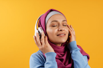 Middle eastern woman in hijab listening music with headphones