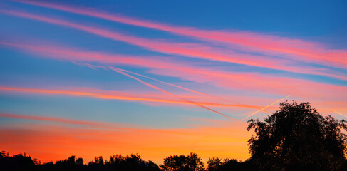 Fototapeta na wymiar Himmel mit orangenem Sonnenuntergang und pinken Kondensstreifen, in Panoramaform