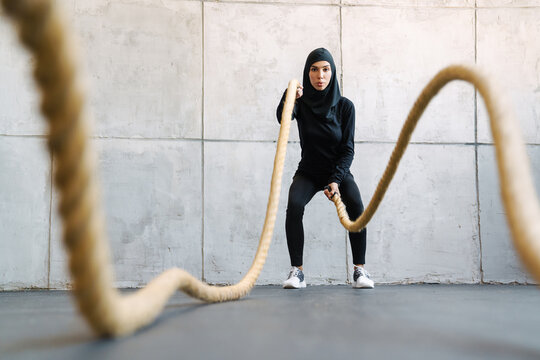 Young Muslim Woman In Hijab Working Out With Battle Ropes Indoors