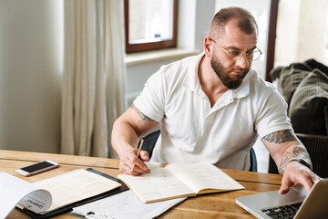 White man in eyeglasses working with papers and laptop