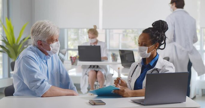 Female doctor and patient in protective masks talking in clinic