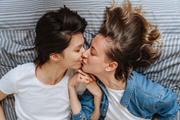 A portrait of the kissing lesbian couple girls holding hands on the bed