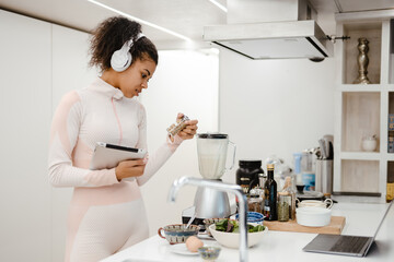 Black woman in headphones using tablet computer while cooking at home