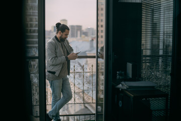 Portrait of a young handsome man with a phone at the window overlooking the city.