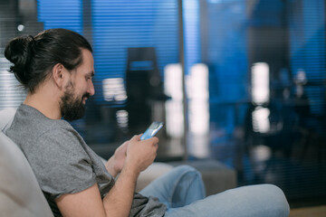 A young man is sitting on the couch with the phone in the evening.