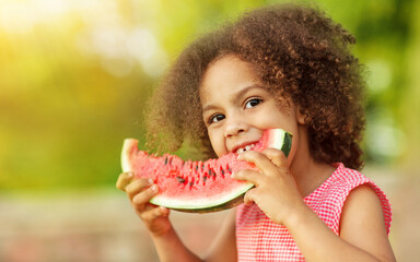 Cute Black girl eating watermelon outdoors in hot summer. Smilhing baby looking at camera, healthy food