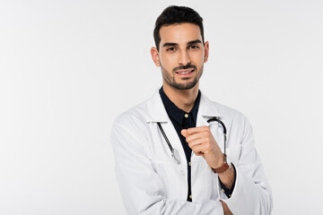 Positive arabian doctor in white coat looking a camera isolated on grey