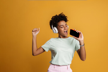 Young black woman listening music with headphones and singing