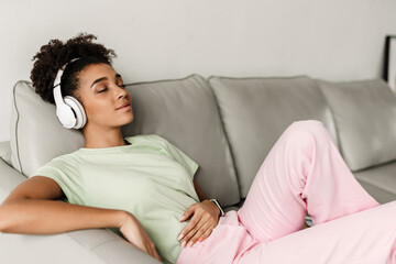 Young black woman listening music with headphones while sitting on couch