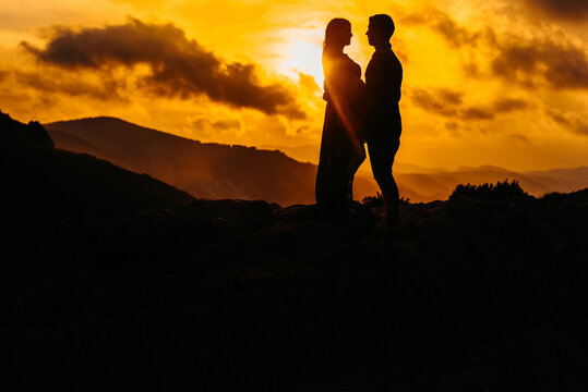 Pregnant woman with husband contemplating sunset in mountains