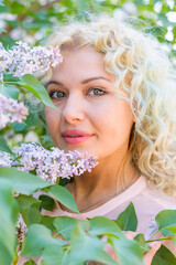Obraz premium A beautiful young and happy blonde girl stands next to a blooming lilac tree. Relaxation in the spring garden.