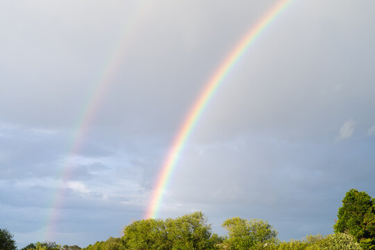 Double rainbow with blue sky background and clouds.