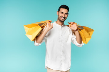 Smiling arabian man holding shopping bags and looking at camera isolated on blue