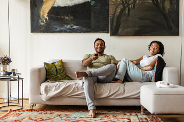 Middle eastern man and woman watching TV while resting on couch at home
