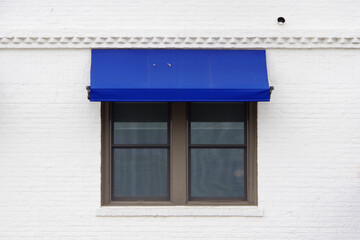 A closed window with a blue awning in a white pained brick building facade