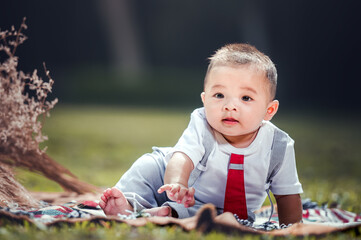 A little boy is sitting on a cloth spread on the grass in the park. 6 month old boy.