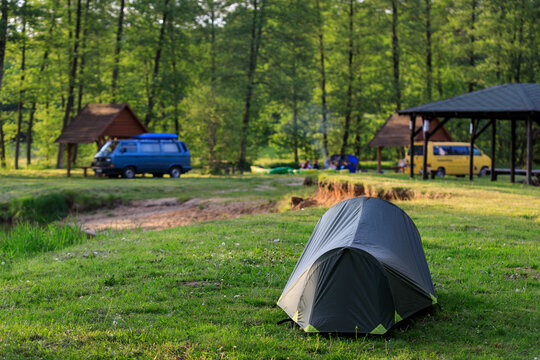 Camping green tent in forest camsite near river on the sunny evening