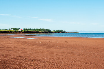 Scenic view of red sand of Prince Edward Island with water, cottages and trees