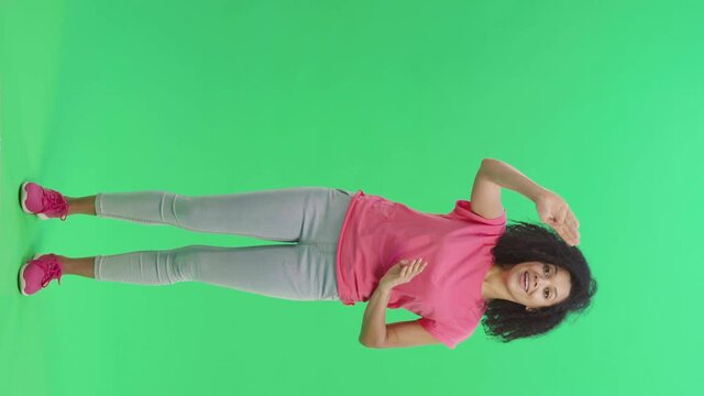 Portrait of young female African American waving hand and showing gesture come here. Black woman with curly hair poses on green screen. Slow motion ready 59.97fps. Vertical video. Full length.