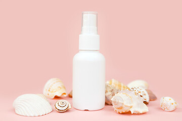 Unbranded white plastic spray bottle and a lot of different sea shells on pink background. Mockup. Skincare beauty and liquid antibacterial spray concept. Mini travel version.