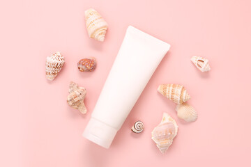 Unbranded white squeeze bottle cosmetic tube and a lot of different sea shells on pink background....