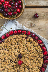 Cherry pie with sprinkles, cherry crumble, and a bowl with fresh cherries on a rustic wooden background, vertical, top view