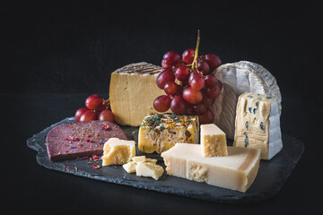 Variety of exclusive and colorful cheese, decorated with red grapes, on black background