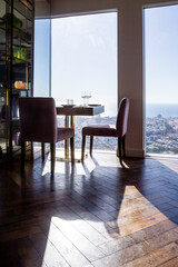served table with armchairs in a restaurant or cafe with a panoramic window overlooking modern city buildings and the sea on a sunny day