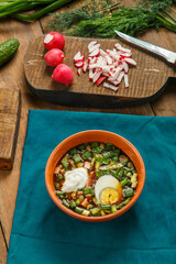 Okroshka in a clay bowl on a table on a wooden table.