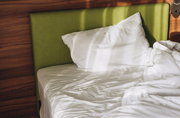 On a bed in bedroom the rays of the sun fall. Comfortable bed with white linen at home