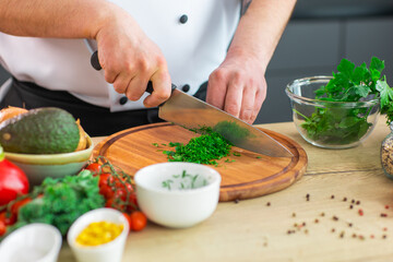 Young chef is cutting herbs and parsley in a modern kitchen. The man prepares food at home. Cooking healthy and tasty food.