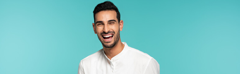 Happy arabian man looking at camera isolated on blue, banner