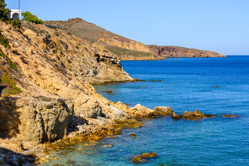 Rocky cliffs on the coast of Piso Livadi. Beautiful bay with blue ocean water. Paros, Greece - obrazy, fototapety, plakaty