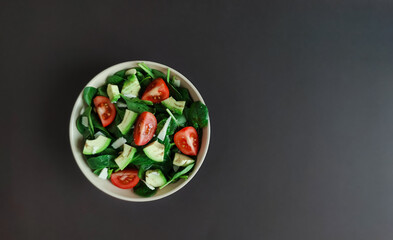 Bowl of salad with spinach, avocado, cherry tomatoes, pumpkin seeds, parmesan on the brown background