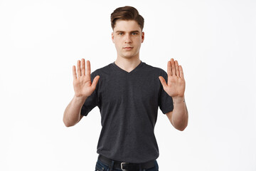 Stop it. Young caucasian man raising hands in block, decline gesture, rejecting or prohibit...