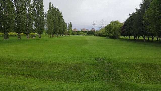 maintained lawn between rows of grown trees. Urban neighbourhood in background. Golf course in town