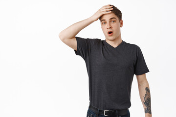 Surprised young man holds hand on forehead, forgot remember something, staring shocked, understood...