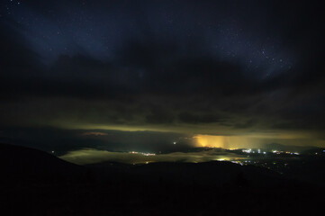 Starry sky with rain clouds and fog in a mountain village