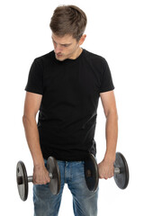 Young handsome tall slim white man with brown hair holds dumbbells looking down in black shirt in blue jeans isolated on white background