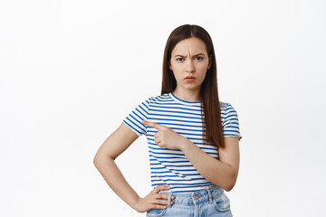 Upset young woman complain, pointing finger left at sale banner, furrow eyebrows and looking...