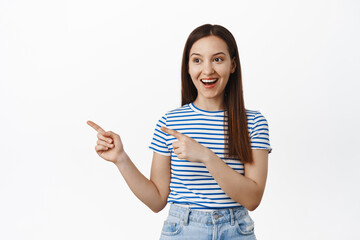Happy girl client pointing fingers and looking left at sale banner, showing advertisement, laughing and smiling at event logo, standing against white background