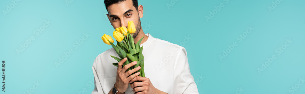 Poster arabian man covering face with flowers isolated on blue, banner