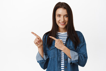 Portrait of smiling woman pointing fingers left, showing logo or banner on empty space,...