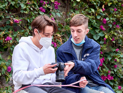 A shallow focus shot of two young Caucasian males watching photos on camera in the park