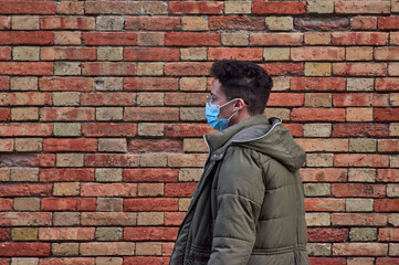 A portrait of a young Hispanic male in a medical mask against a brick wall