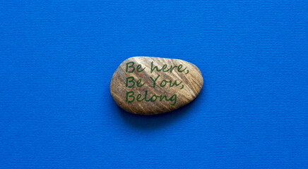 Be here, be you, belong symbol. Beautiful stone with words 'Be here, be you, belong' on beautiful blue background. Diversity, business, inclusion and belonging concept.