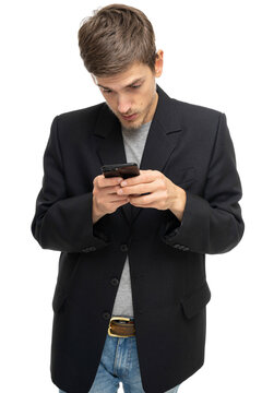 Young handsome tall slim white man with brown hair is looking to his mobile phone in black blazer isolated on white background