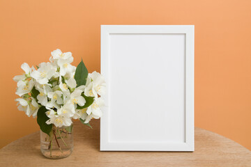Fototapeta na wymiar Mock up empty white frame on a round table with jasmine flowers on orange background. Place your text or image