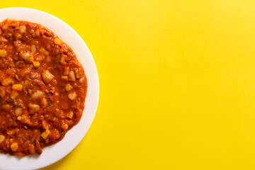Traditional Hot chili sauce. Chopped meat, white beans, korn pepper, paprika in a tomato sauce. on a white plate and a yellow background