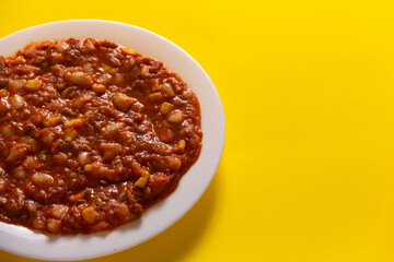 Traditional Hot chili sauce. Chopped meat, white beans, korn pepper, paprika in a tomato sauce. on a white plate and a yellow background